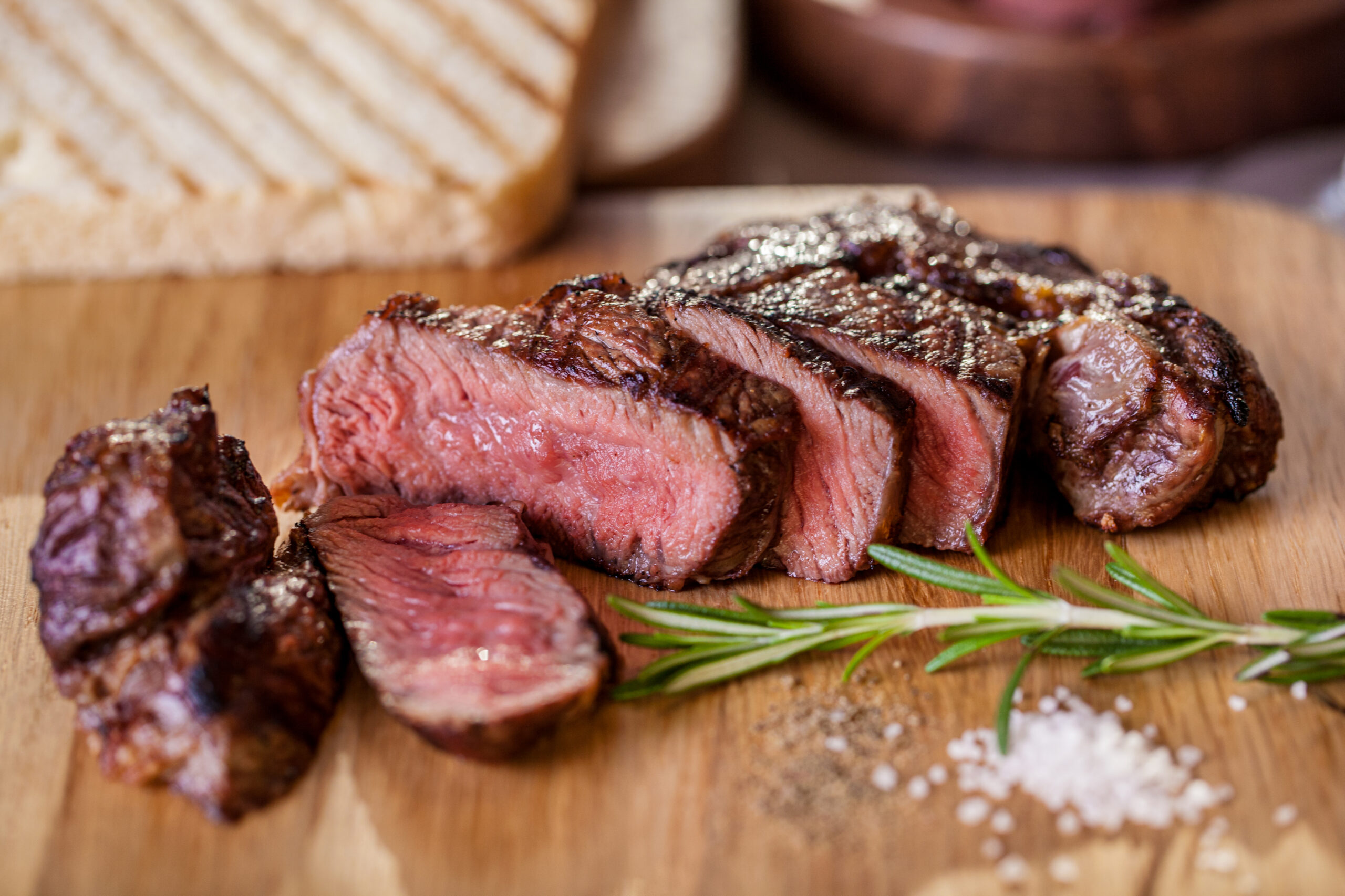 Grilled pork steak pieces with a sprig of rosemary, pepper and salt, fried pieces of bread on a wooden board. Horizontal orientation