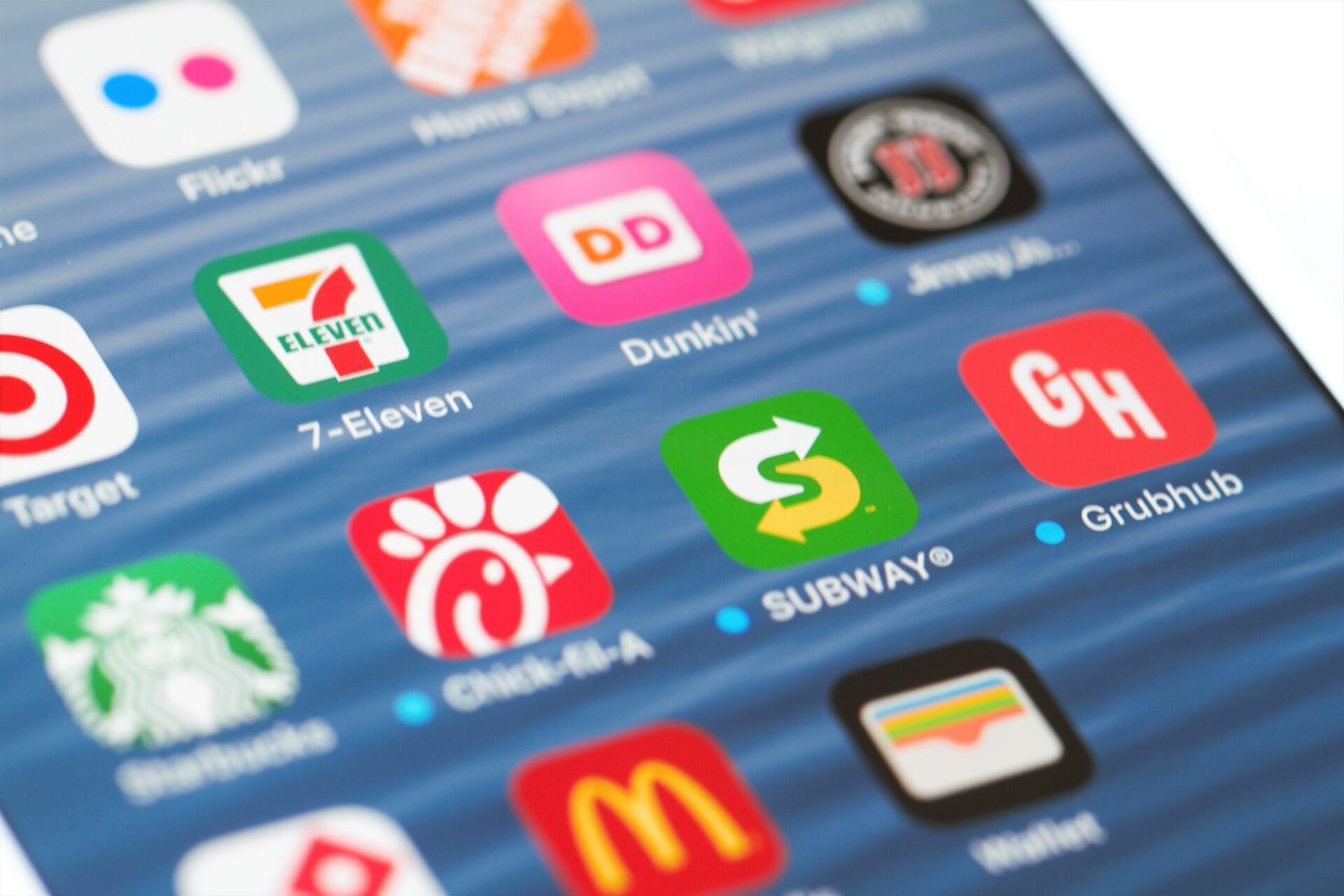 Grouping of popular restaurant mobile apps on an iPhone screen. Apps include fast food restaurants such as Starbucks, Subway, Chick-fil-A, Domino's, Dunkin Donuts and Jimmy Johns as well as Target, Home Depot and meal delivery site Grubhub. Selective focus on middle row of apps and side angle view.