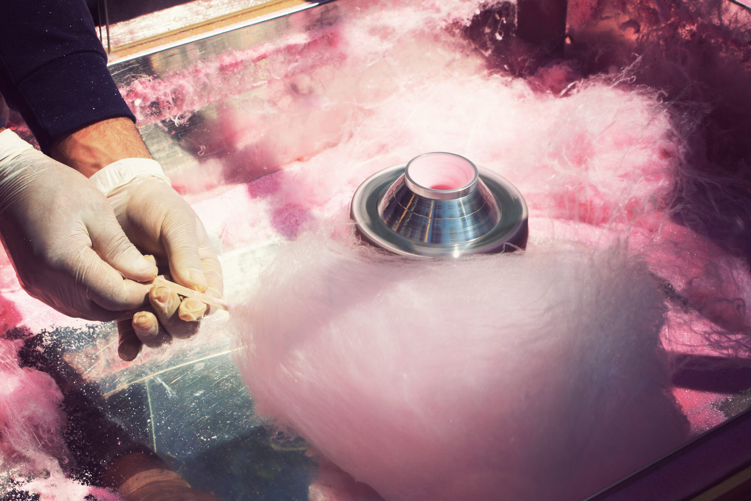 hands rolling filaments of pink sugar to make a cotton candy cone