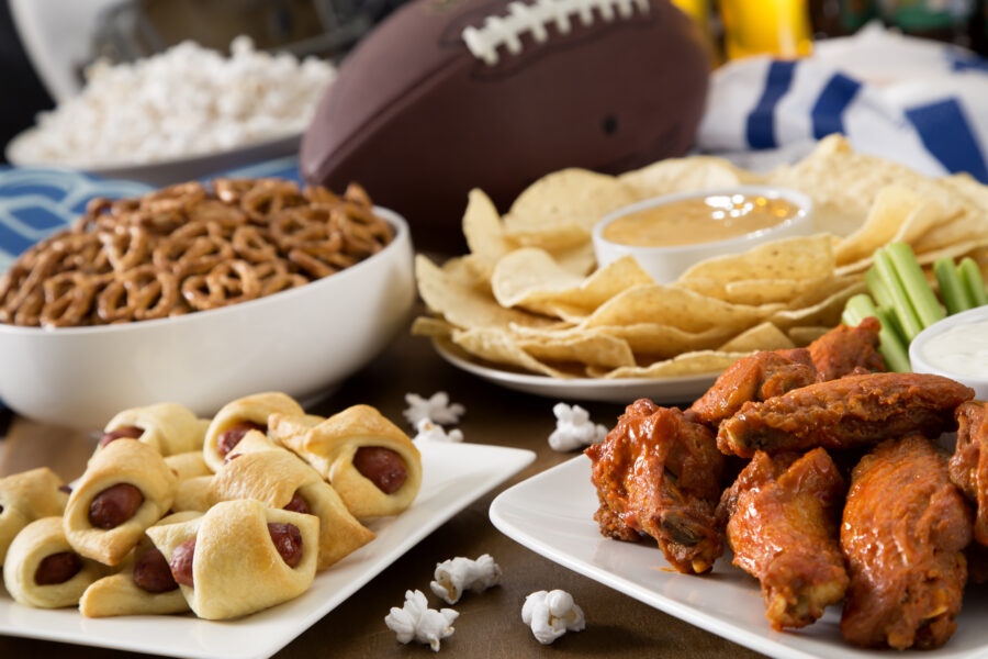 Hot wings, nachos, pigs in a blanket, beer, and popcorn, a tailgate party spread.  