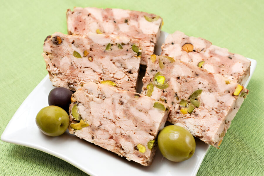 Traditional French terrine with olives on a white plate on a green background