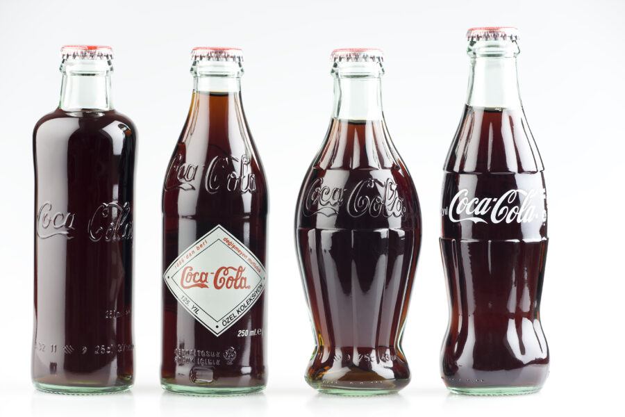 Four Coca-Cola bottles side by side ; (1899-1900-1915-1957 editions) 125 years old anniversary edition, studio shot.