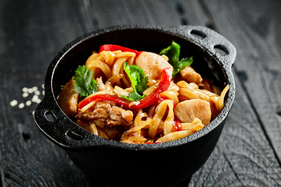 Japanese stir fryed udon noodles in wok. Udon noodle with chiken and vegetables on wooden background. Asian noodles on black table with ingredients. 