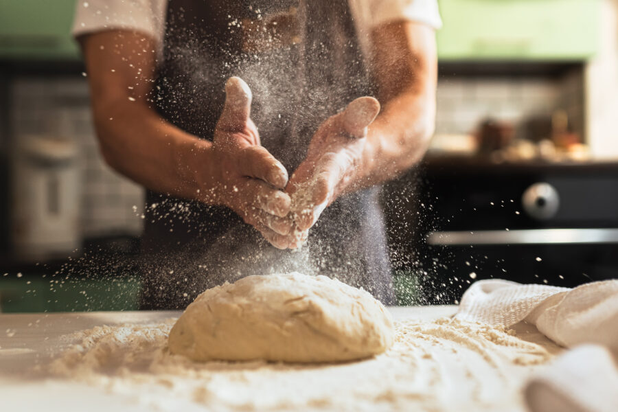 Male chef in kitchen chef's apron spraying flour over dough