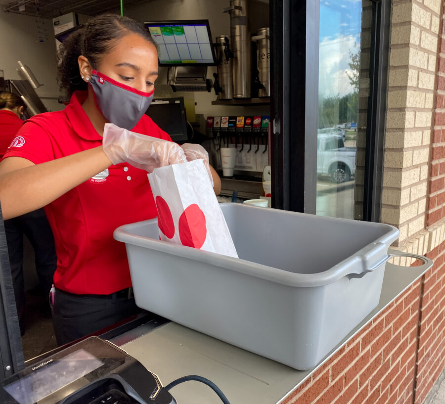 Chick-fil-A employee wears mask and glove packing food for customers at the service window during covid 19