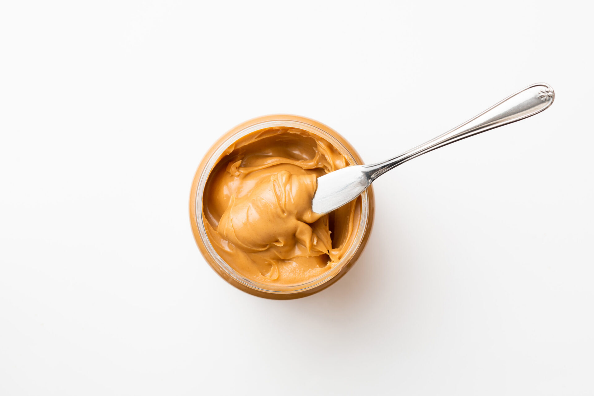 Open jar of peanut butter with spoon.