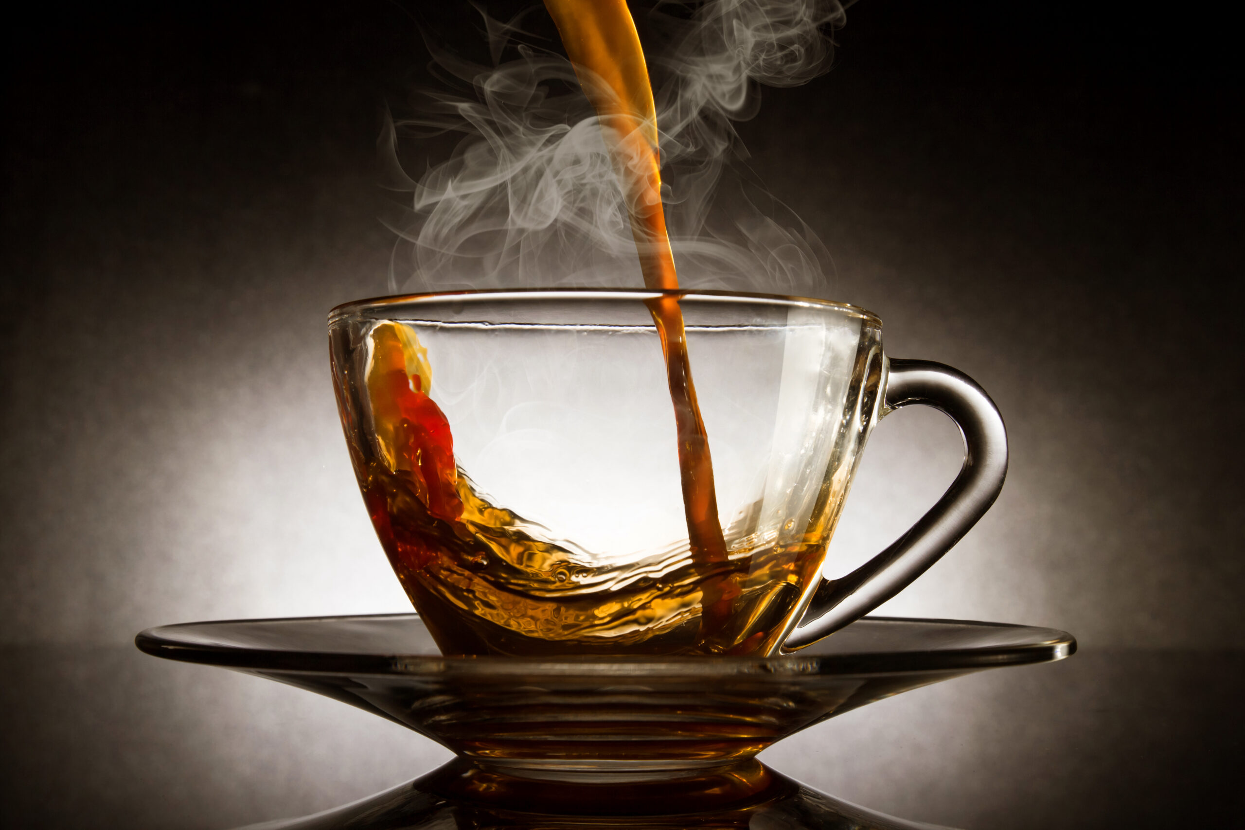 Pour coffee into transparent glass with steam cup on dark background.