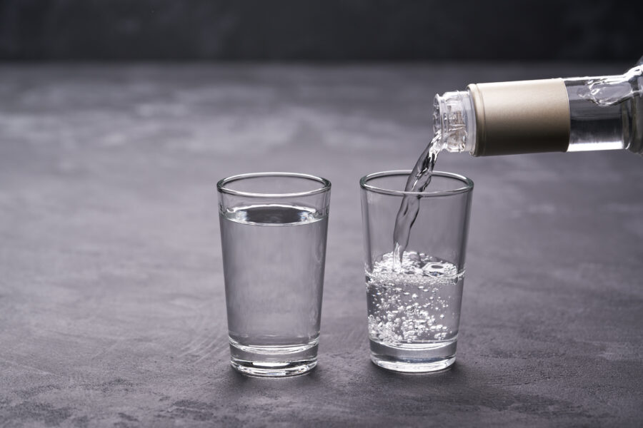 Pouring vodka into the glass on a black background, selective focus