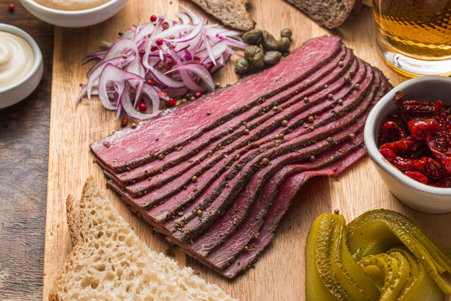 Sliced Deli Pastrami on wooden board, flat lay.