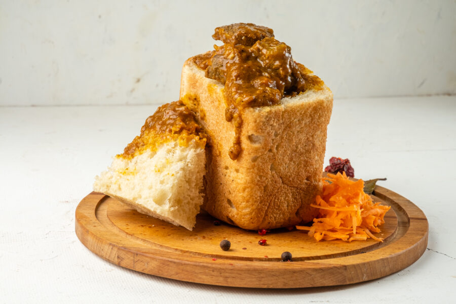 South African fast food dish bunny chow curry with meat and vegetables in white bread on a light background.