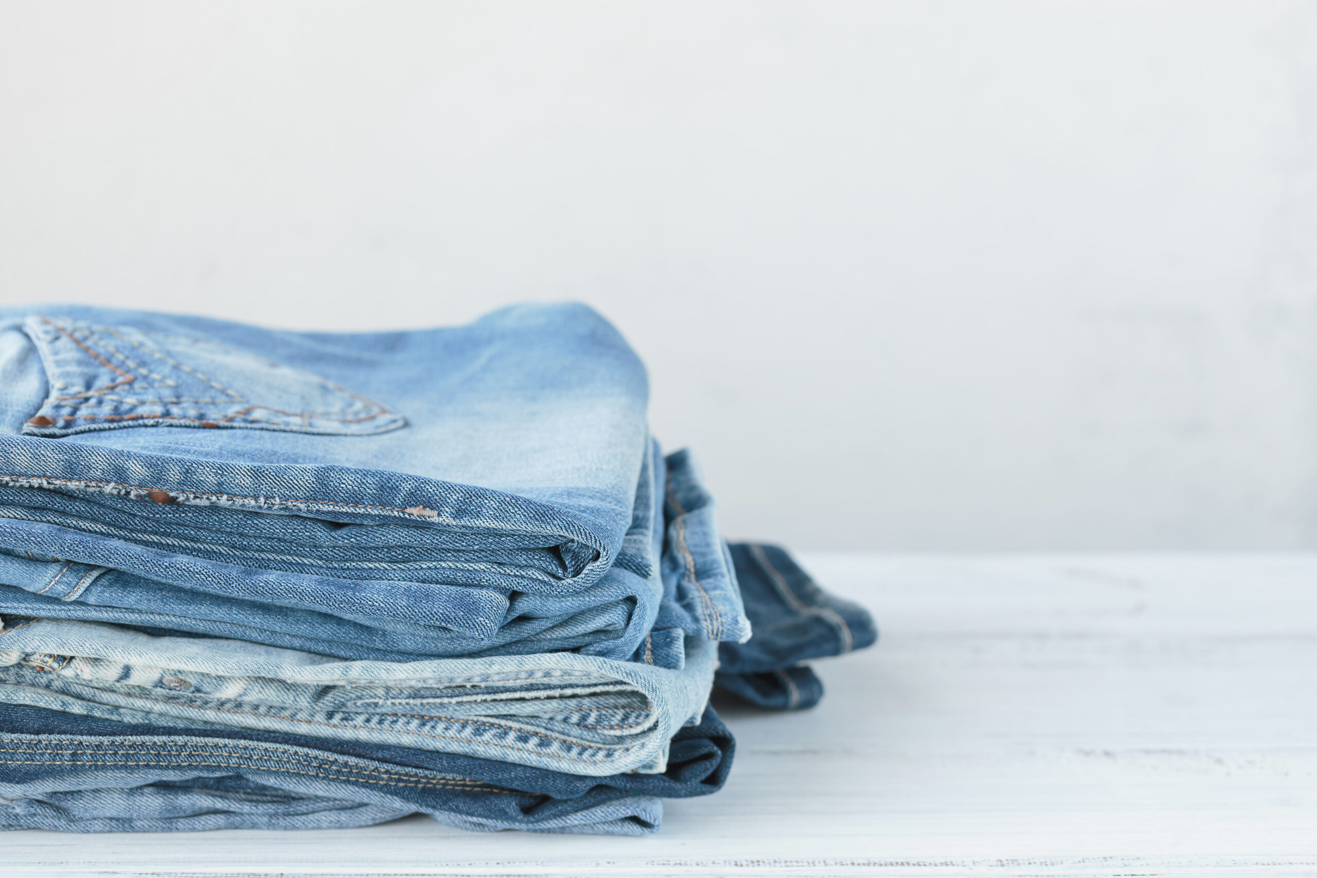 Stack of blue jeans on white background. Second hand clothing shop. Circular fashion, eco friendly sustainable shopping, thrift stores concept. Free copy space for text.