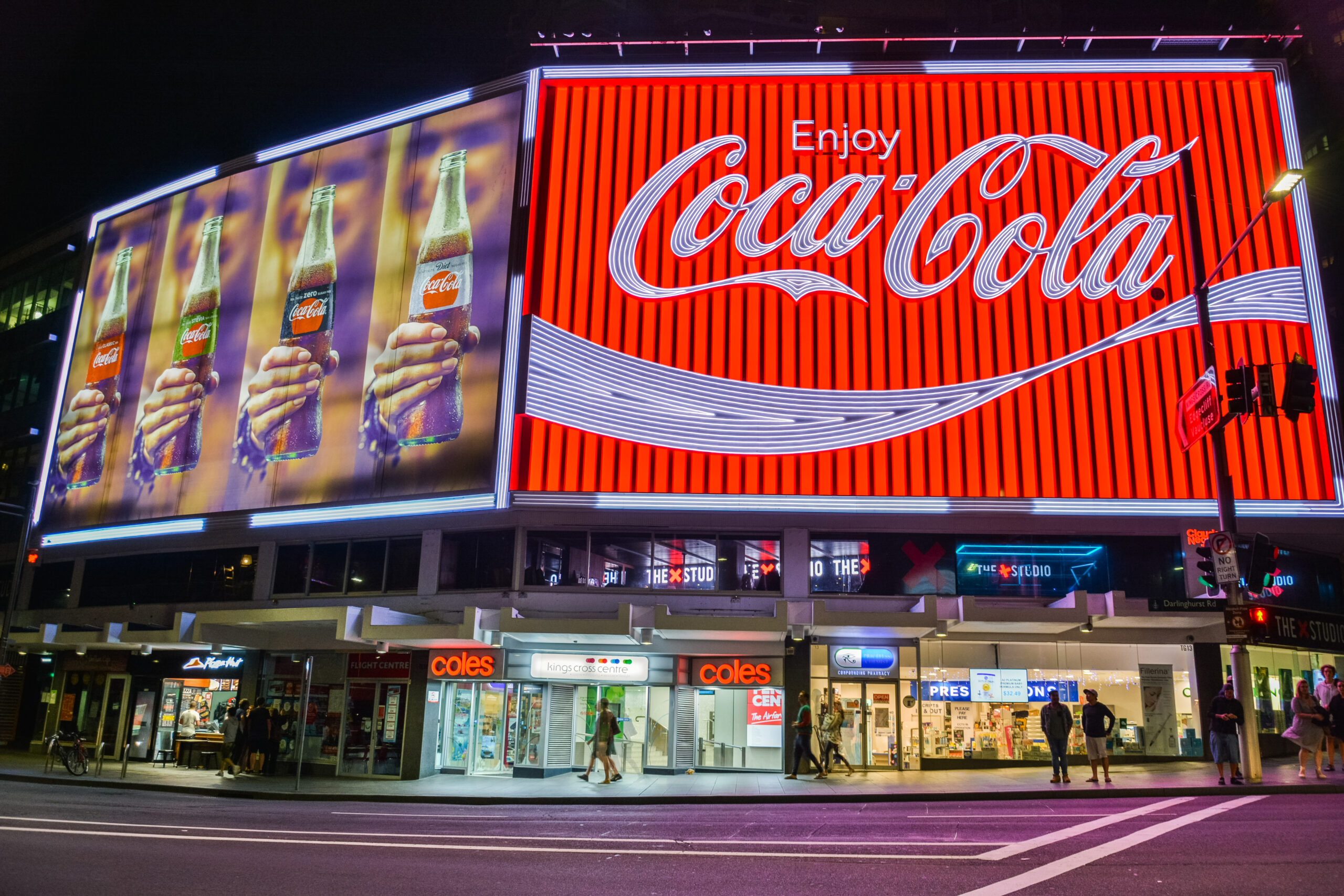 The Coca-Cola Billboard in Kings Cross, Sydney, with commercial properties and people, at night.