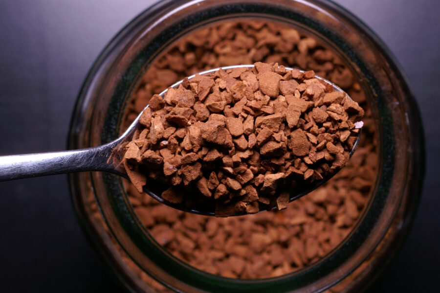 Teaspoon of instant coffee from above with the jar of coffee below.