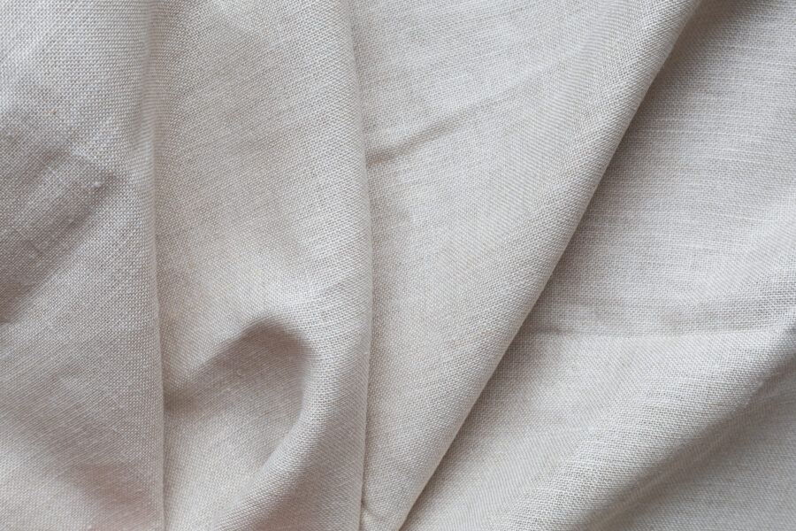 Textured folds of linen fabric in natural beige color. Textile background, top view, copy space