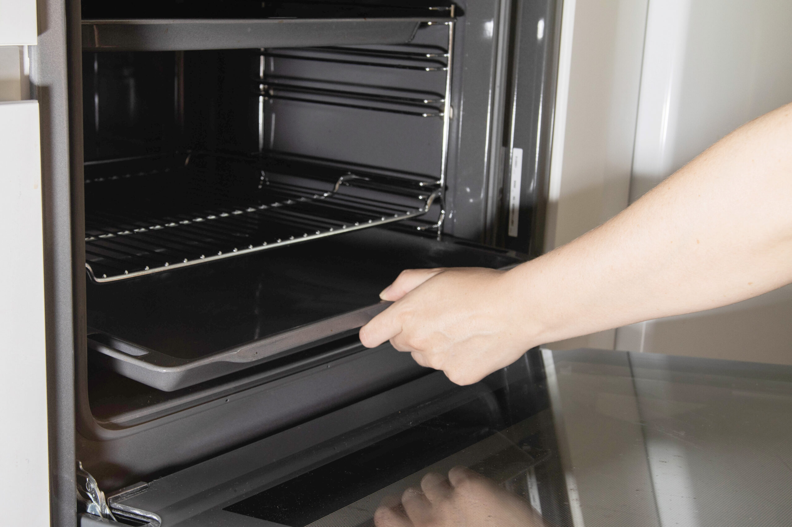 The girl takes out a metal baking sheet from the stove oven to clean it. Care and cleaning of the oven, hygiene