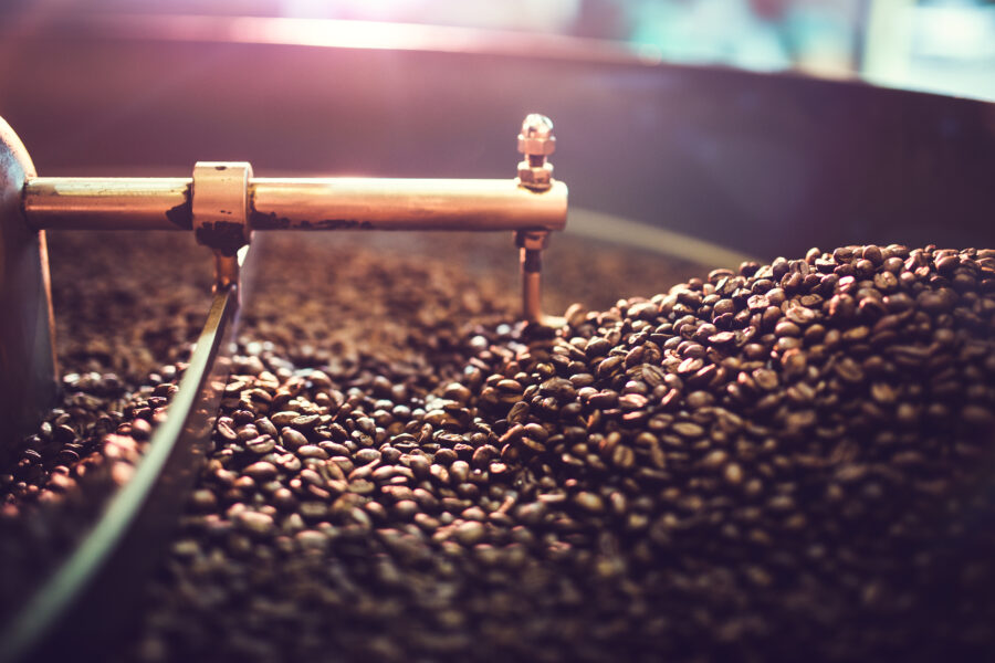 The process of roasting a batch of high quality single origin coffee beans in a large industrial roaster; the toasted beans are in the cooling cycle.  Horizontal image with copy space.  High contrast with colorful tones.