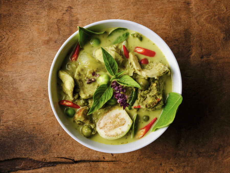 This Thai known in Thai as 'Gaeng Keow Wan Gai' dish is very famous and known all over the world and one of Thailand's popular signature dishes when it comes to Thai food. This dish consists of ingredients including a green herb-based base with fresh coconut milk, sweet basil, Thai aubergines, pea aubergines, chicken, and spicy fresh red chili. The combination of ingredients results in a sweet and spicy taste with a variety of complementary textures and is normally eaten together with fresh steamed Jasmine Thai rice or fresh rice noodles. The image was taken from directly above with the bowl set on an old worn textured wooden background with lots of grain and character.