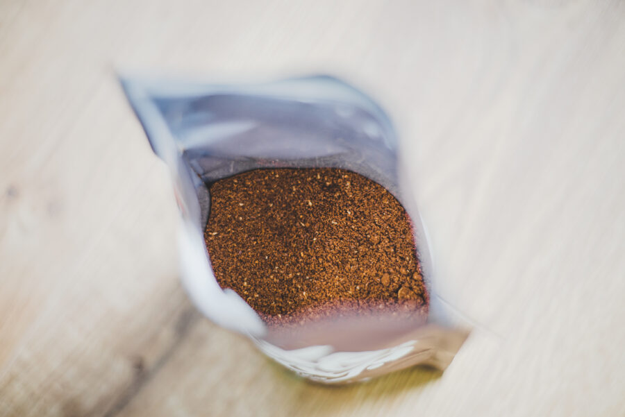 Top view to open plastic pack with medium roasted arabica ground coffee. Focus on coffee. Pack is on wooden base.