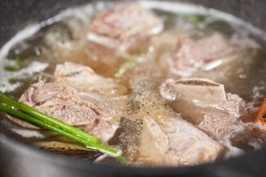 Traditional beef broth with vegetable, bones and ingredients in pot, cooking recipe. Soup in a cooking pot with ladle on dark stone background.