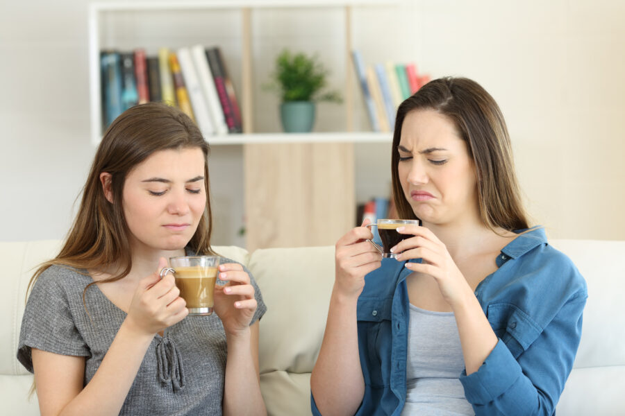 Two friends drinking coffee with bad flavour sititng on a couch in the living room at home