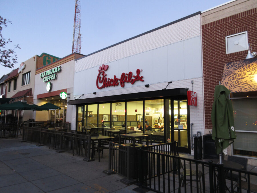 Chick-fil-A and Starbucks next to each other. People inside Chick-fil-A are eating or waiting in line to order food.