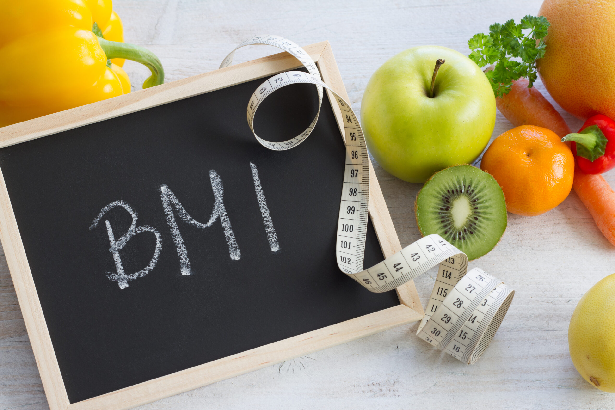 Word BMI on chalkboard. Fruits, vegetables and measuring tape, healthy diet concept background