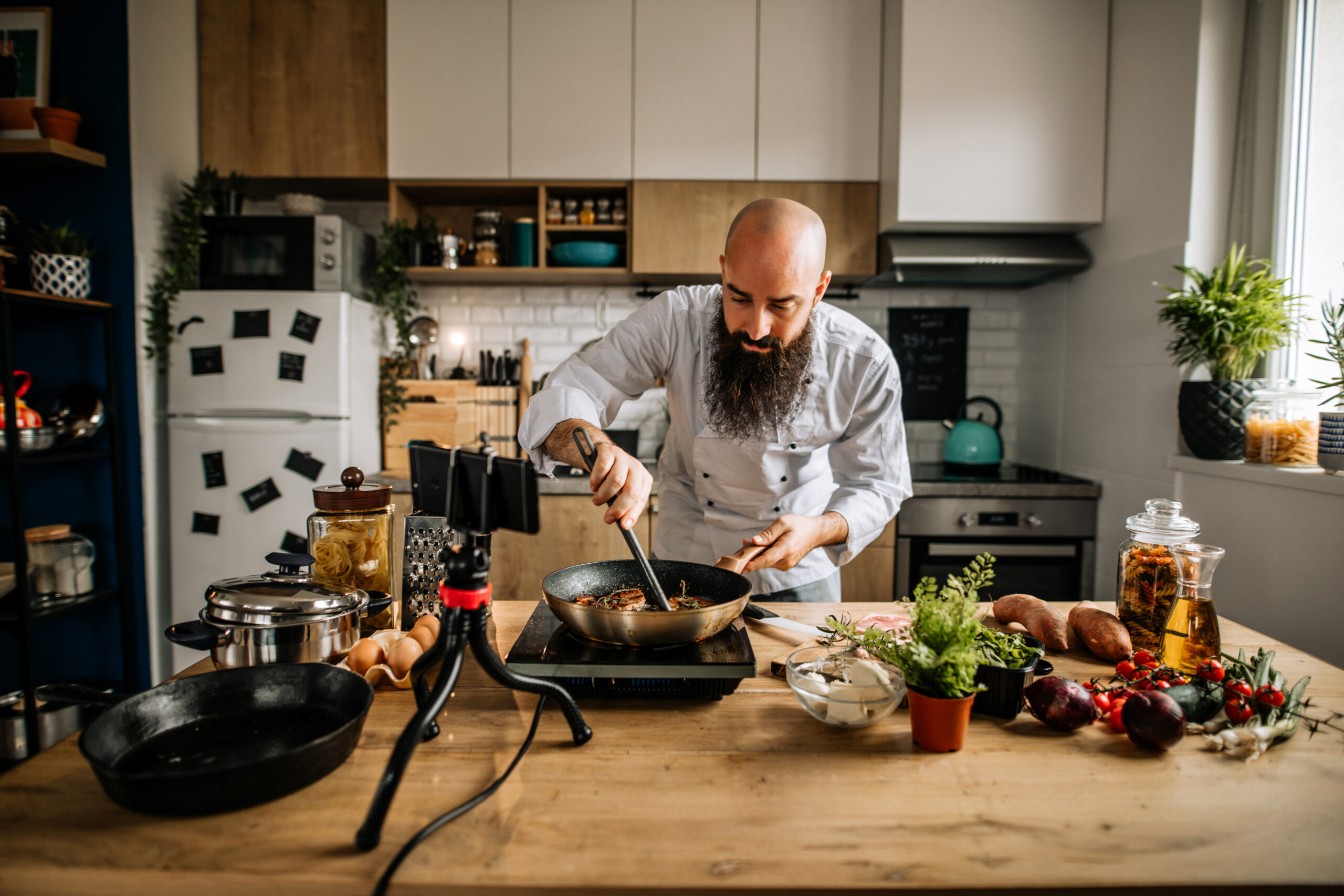 Young bearded chef, food vlogger filming and live streaming steak preparing tutorial in home kitchen