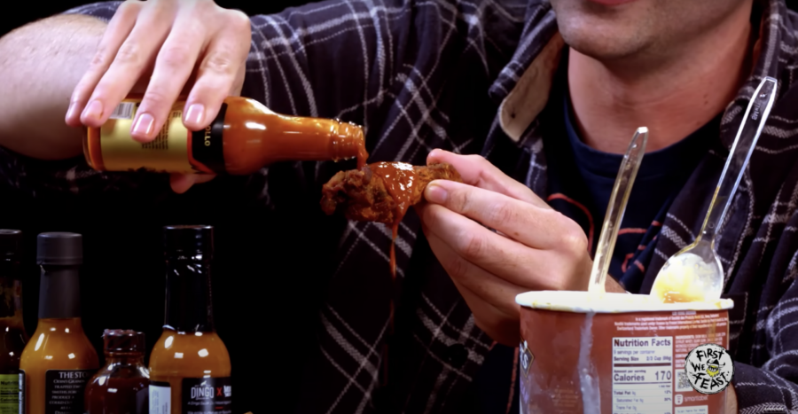 Man pouring hot sauce on a chicken wing. From YouTube video "The Best Last Dab Reactions of 2022 | Hot Ones" by First We Feast