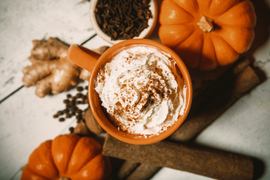 An Autumn favorite hot drink, the pumpkin spice flavored coffee, tea, or chai, complete with fresh pumpkins and whipped cream topping.  Cinnamon sticks, ginger, cloves, and allspice surround the mug of spicy warm goodness.  Rustic wood table.