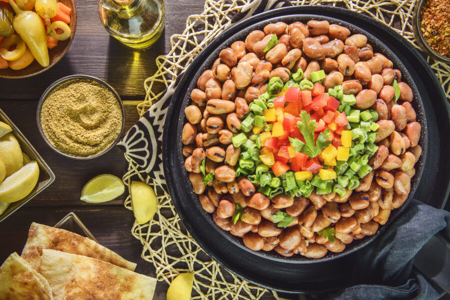 Egyptian traditional dish "Ful medames". Middle Eastern breakfast with cooked fava beans and fresh vegetables. Served with olive oil, pickles, pita bread, cumin and lemon.