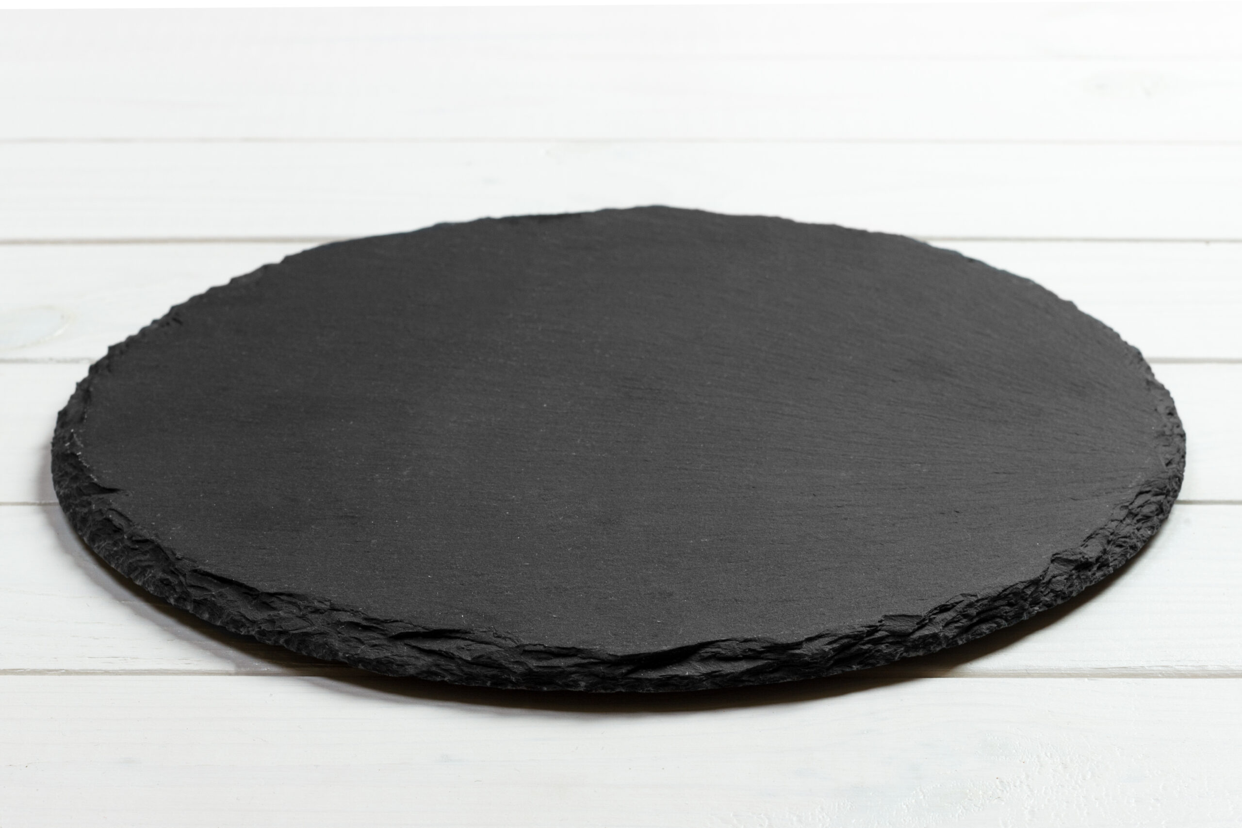 Black slate round stone on wooden background, top view, copy space.