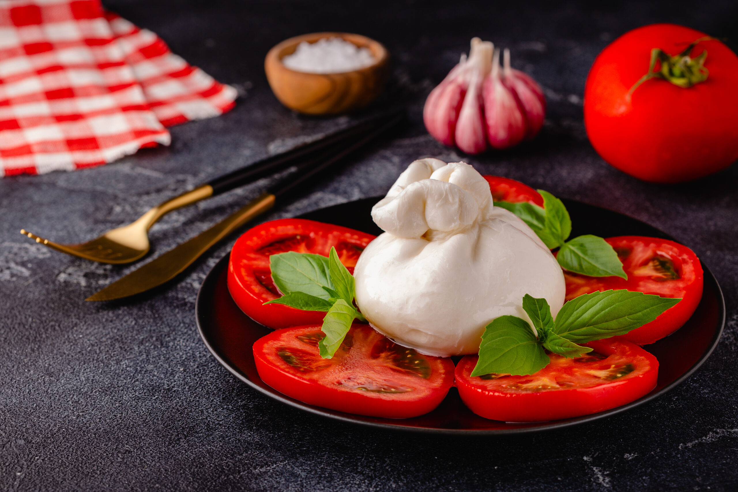 Caprese salad with tomatoes, burrata cheese and basil. Dark background.