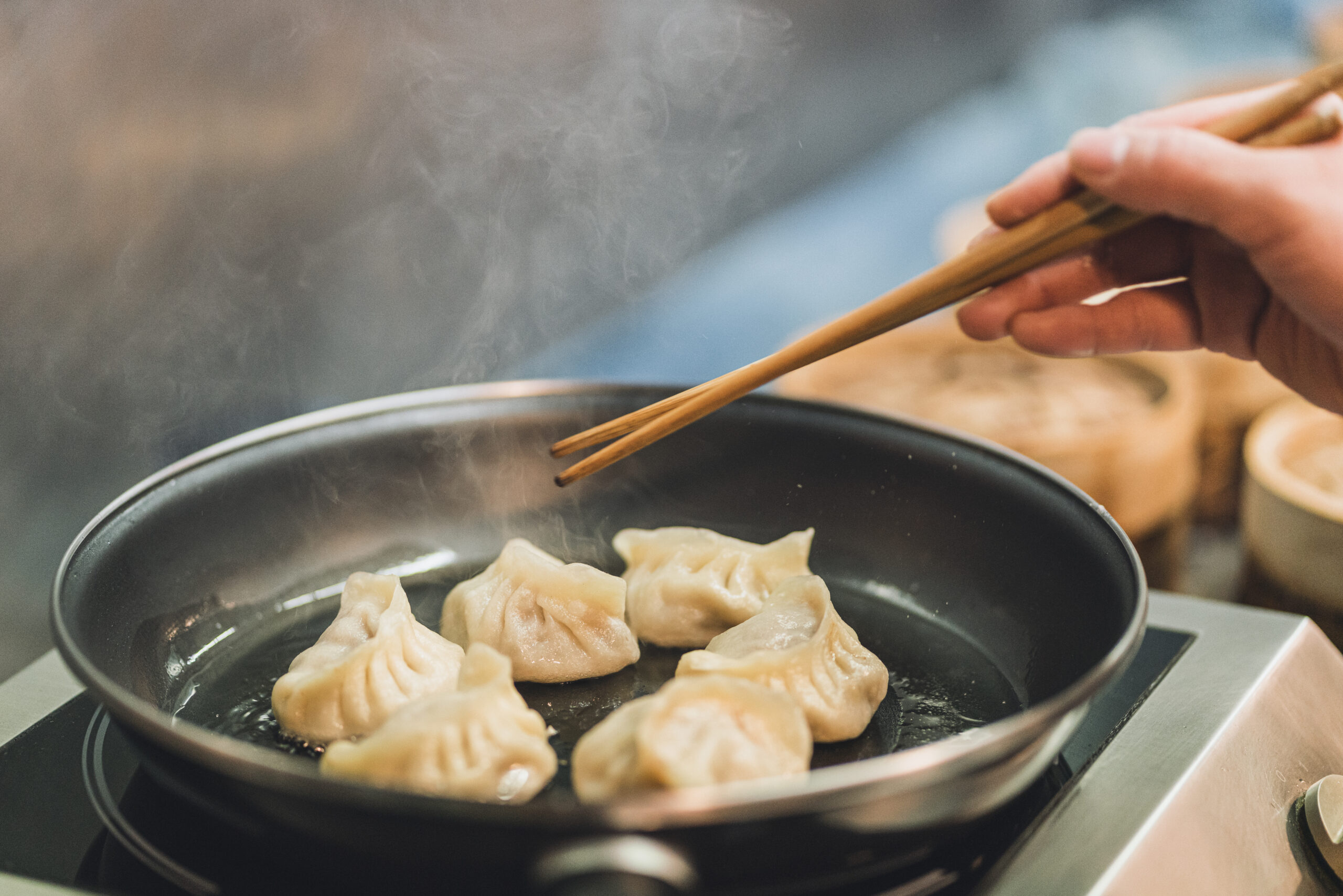 chef is cooking dumplings in a frying pan and moving with chopsticks