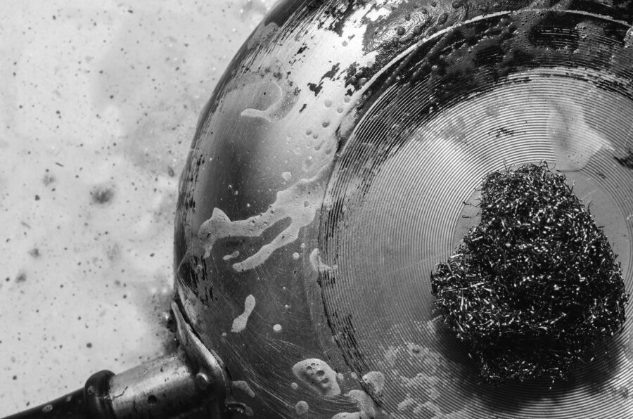 Cleaning ngara in a pan with a metal scraper with detergent, black and white photo, close-up