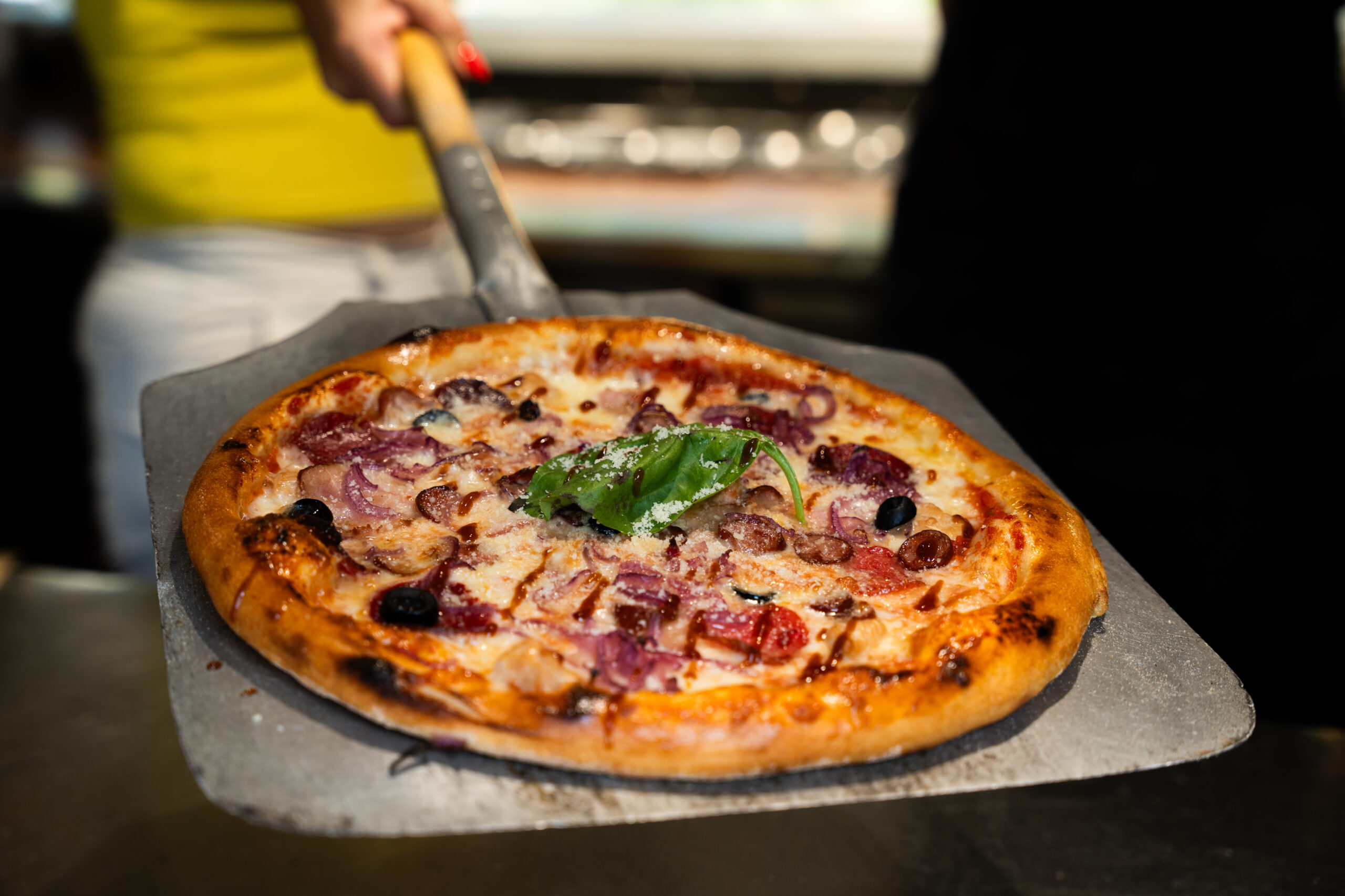 Close-up of a freshly baked artisan pizza with the chef and restaurant interior in the background, out of focus