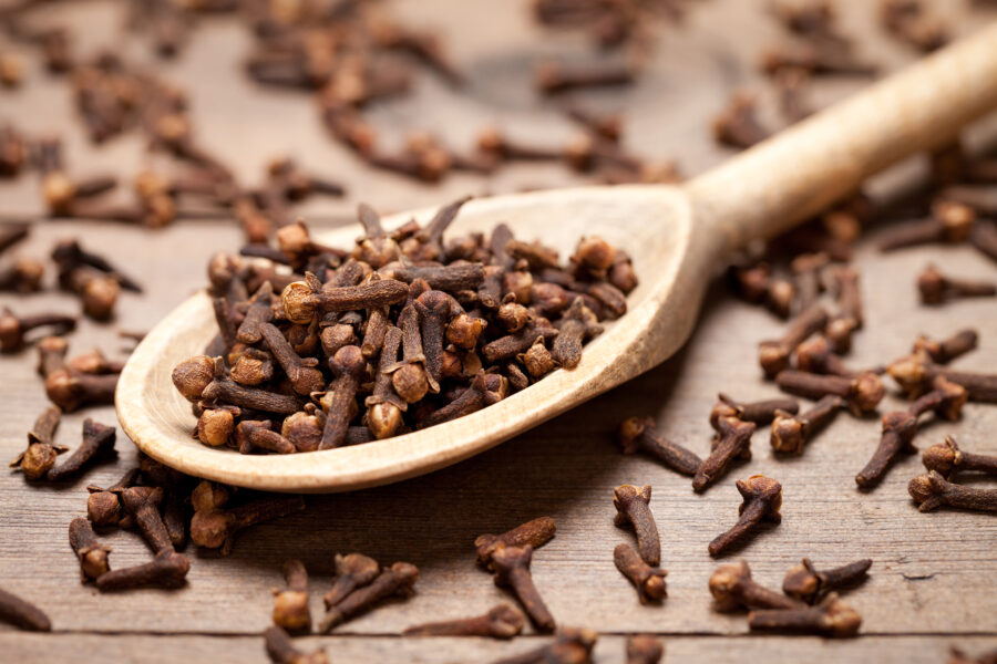 Close up of cloves in spoon on white old wooden table. 