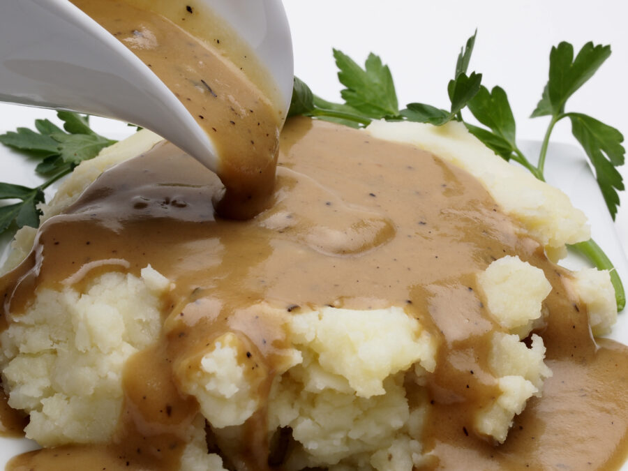 Close up of gravy boat pouring over mashed potatoes