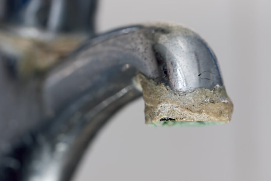 Close-up of limescale build-up. Selective focus on hard water deposit on old tap spout. 