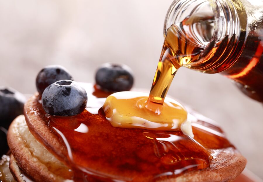 Close-up of pouring maple syrup on stack of pancakes.