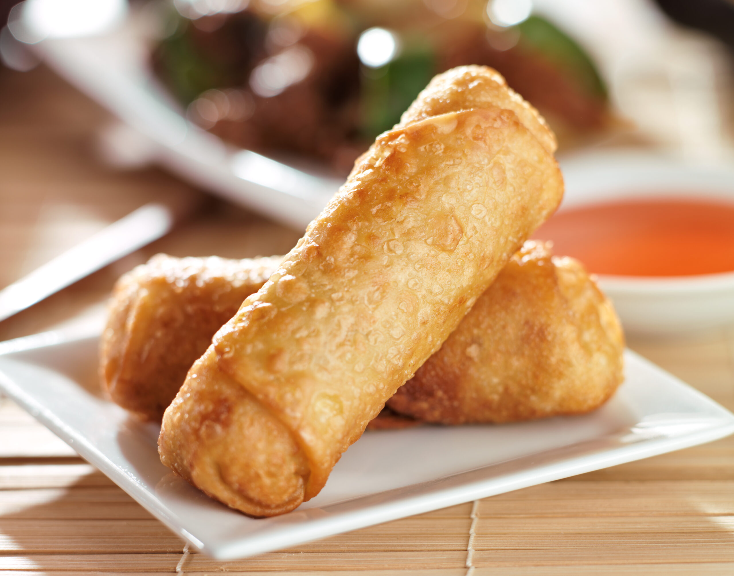 close up photo of chinese egg rolls with sauce on plate