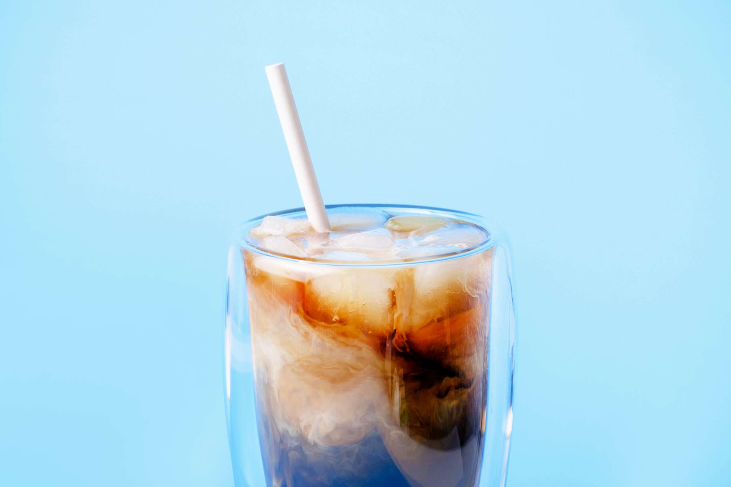 Coffee with milk and ice in a glass cup on a blue background.