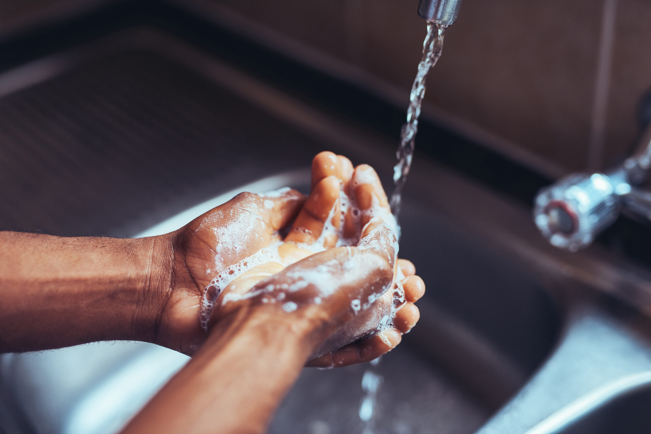 Cropped shot of an unrecognizable man washing his hands in the kitchen sink at home