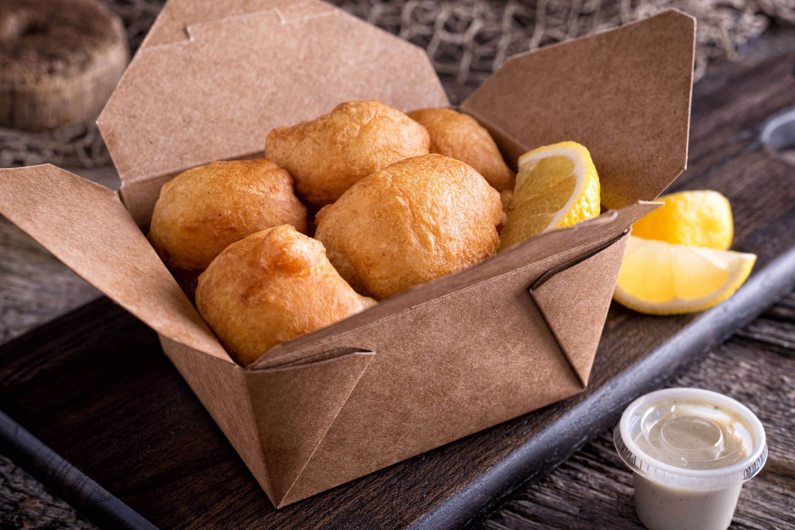 New England style clam fritter cakes in a take out container on a rustic wood table top.