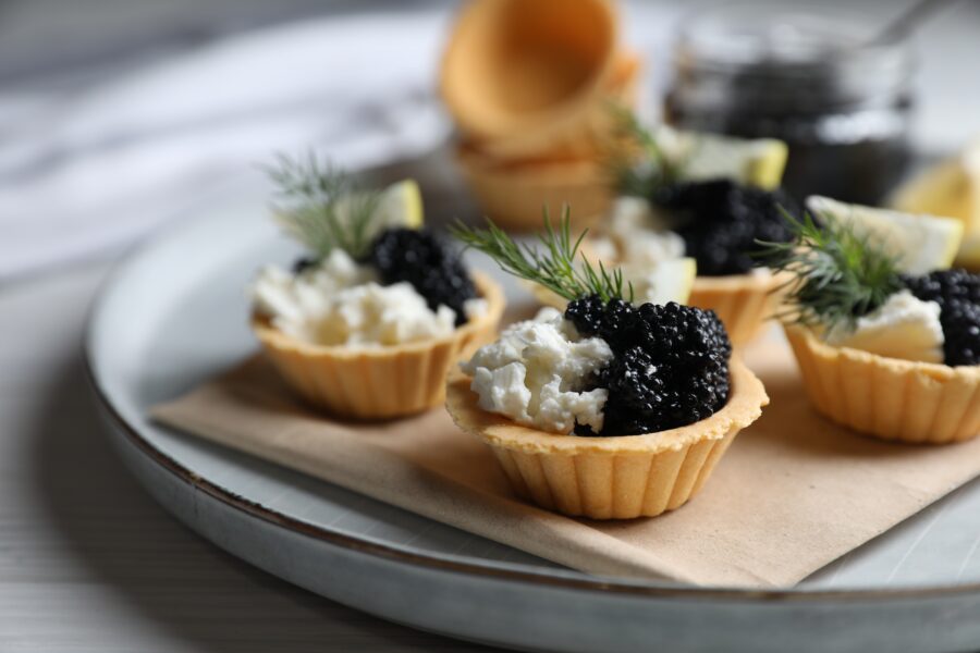 tartlets with black caviar, cream cheese and lemon served on light table, closeup