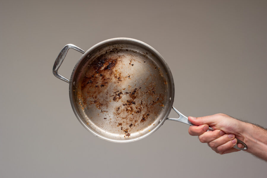 Dirty oily burnt metal frying pan held in hand by male hand. .