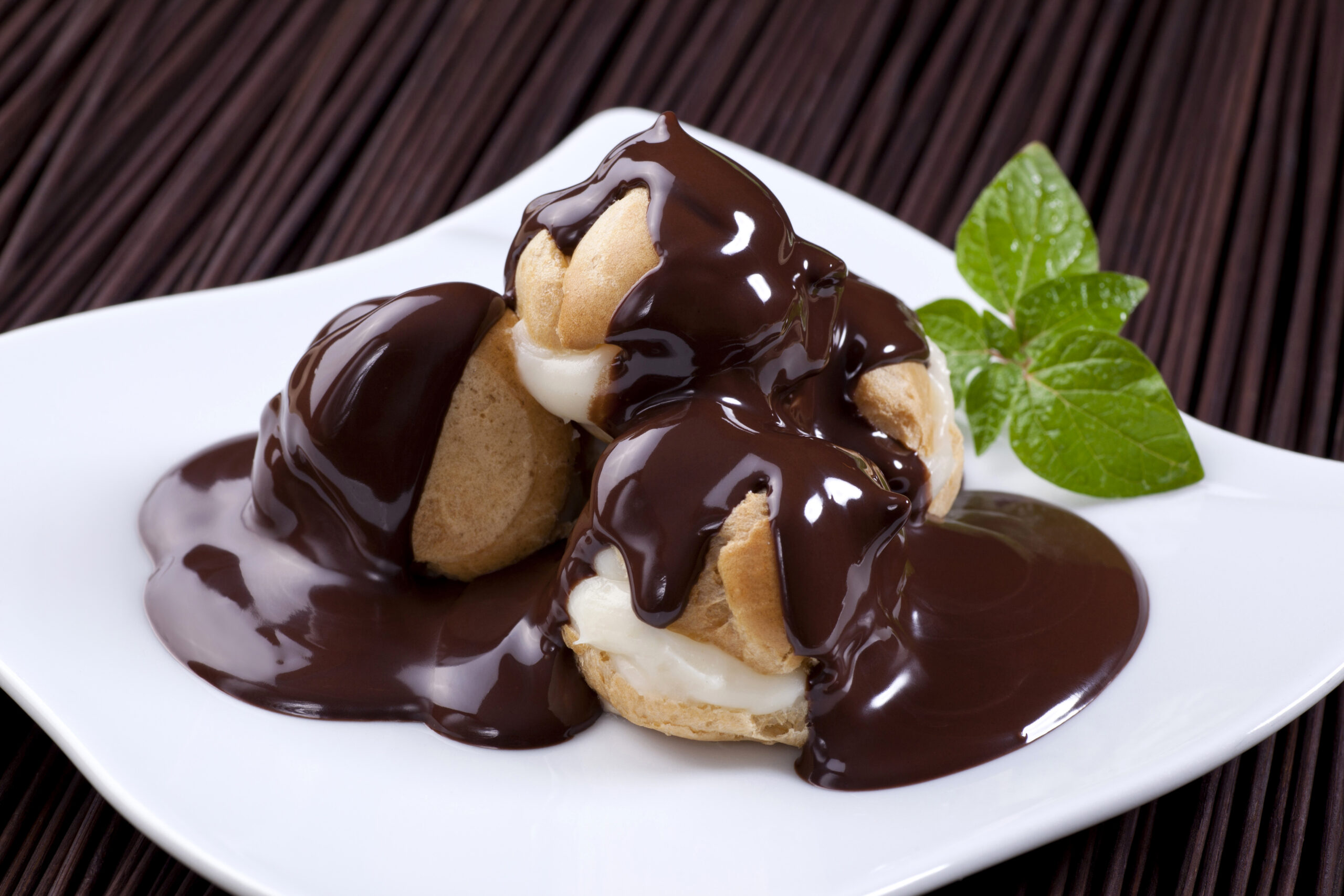 Fresh profiteroles covered with chocolate syrup on a white plate.