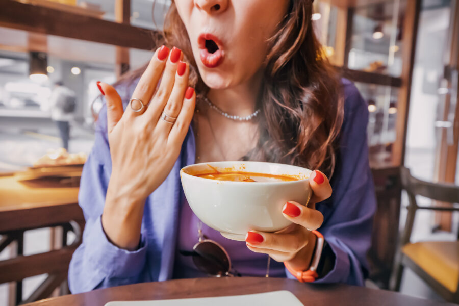 Girl tries a spicy and hot soup in a restaurant and reacts funny.