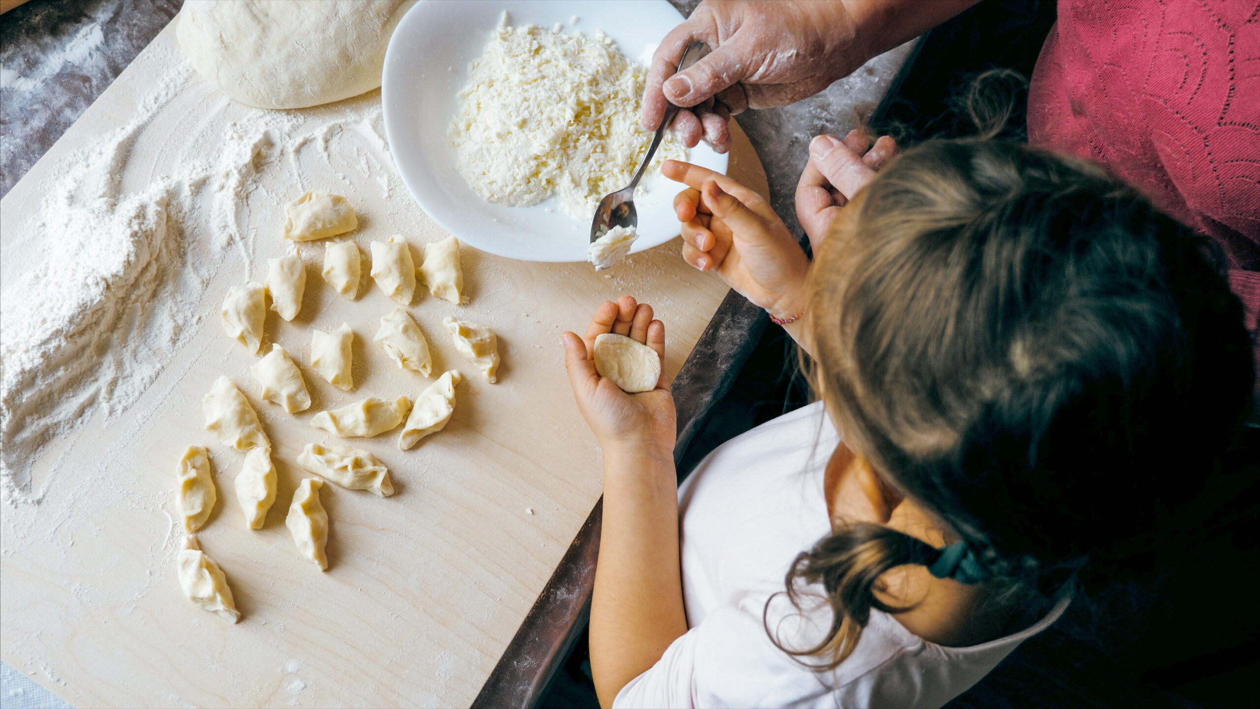 Grandmother with granddaughter is making dumplings with cheese at home kitchen together, view from above