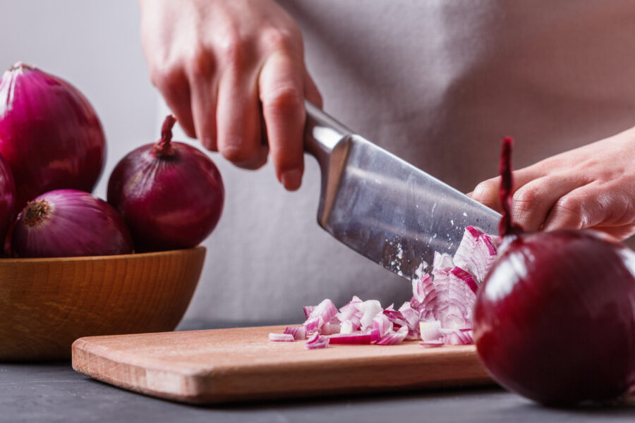 young woman in a gray aprons cuts red onion.