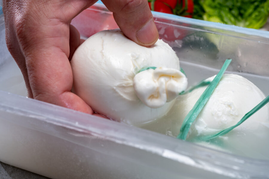 Cheese maker holds in hand Italian cheese, white balls of burrata or burratina cheese made from mozzarella and cream filling